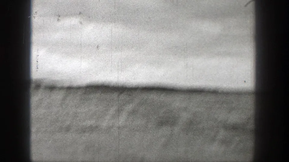 Overexposed Washington coastal view on 8mm film, with a faint shoreline and dark vertical frame shadows.