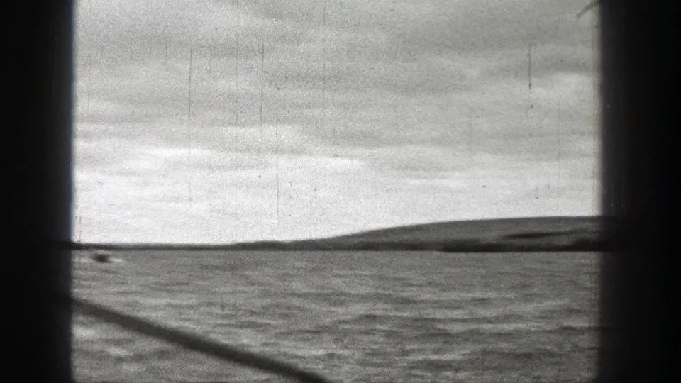 Grainy 1938 Washington coastal frame showing ocean water, a low island-like silhouette, and cloudy sky.