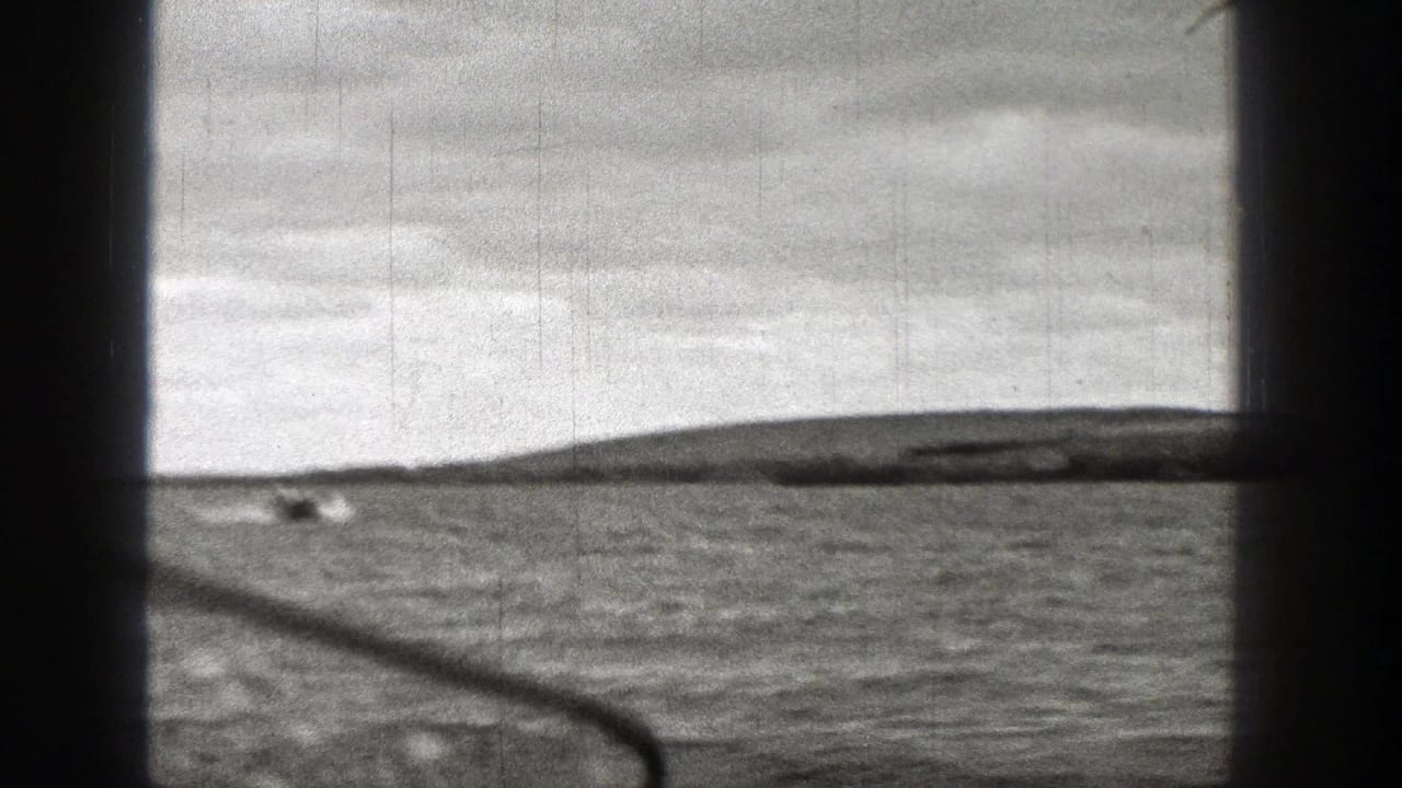 Black-and-white 8mm view of Washington coastal water with distant land on the horizon and visible film scratches.