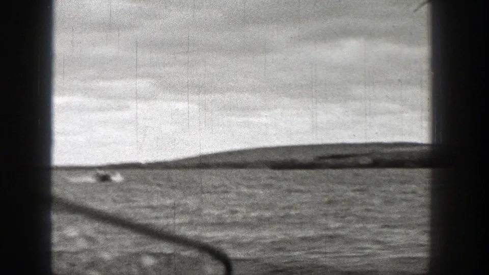 Black-and-white 8mm view of Washington coastal water with distant land on the horizon and visible film scratches.
