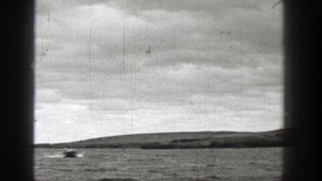 Small motorboat crossing distant water near a low shoreline under cloudy sky.
