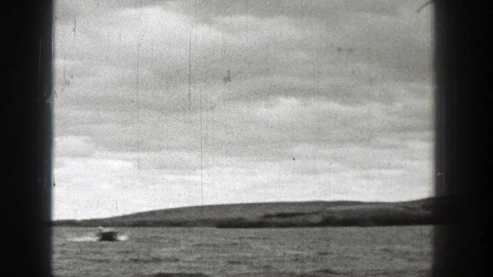 1938 Washington 8mm frame showing a small motorboat far left on open water, with low hills and an overcast sky beyond.