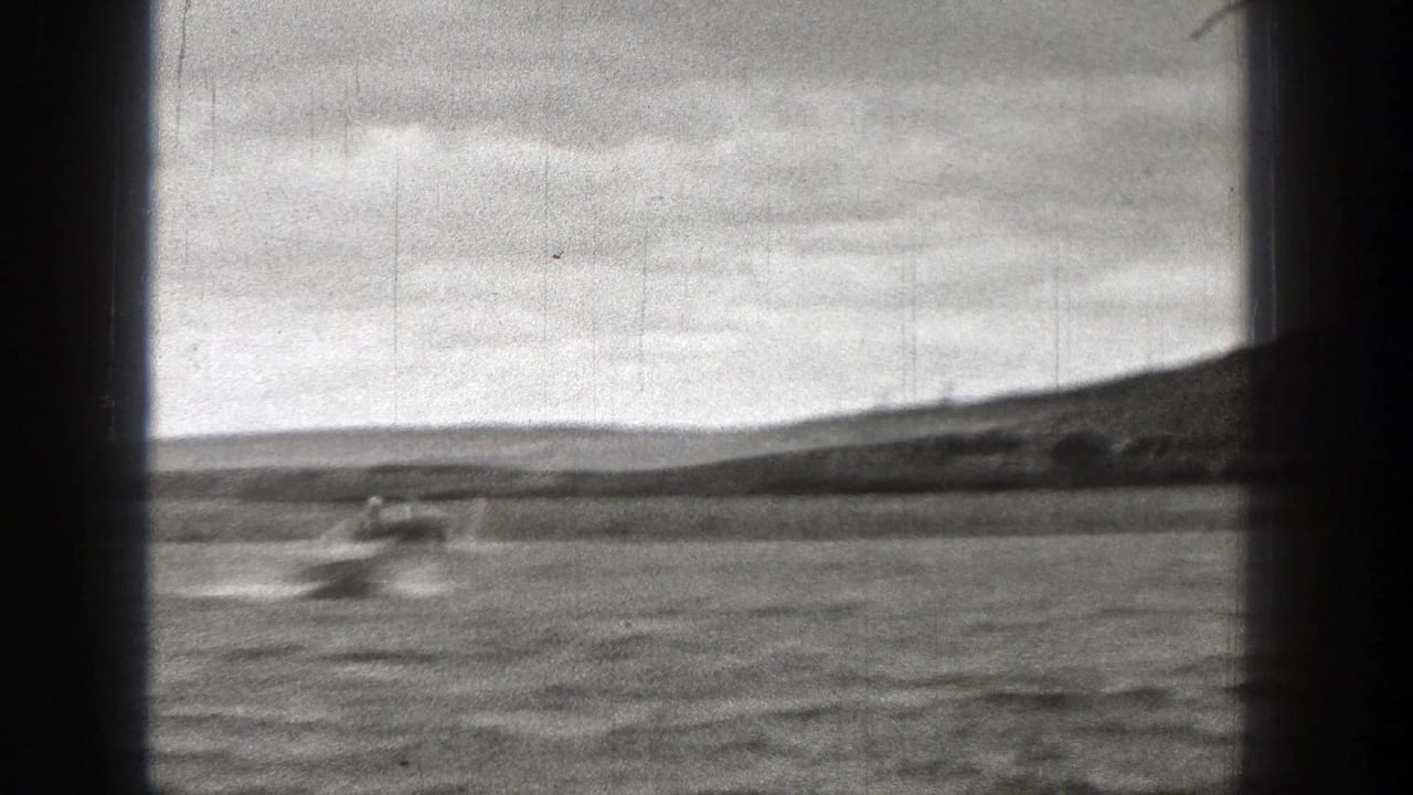 1938 Washington home-movie frame of a small motorboat accelerating across rippled water, leaving a white wake near the horizon.