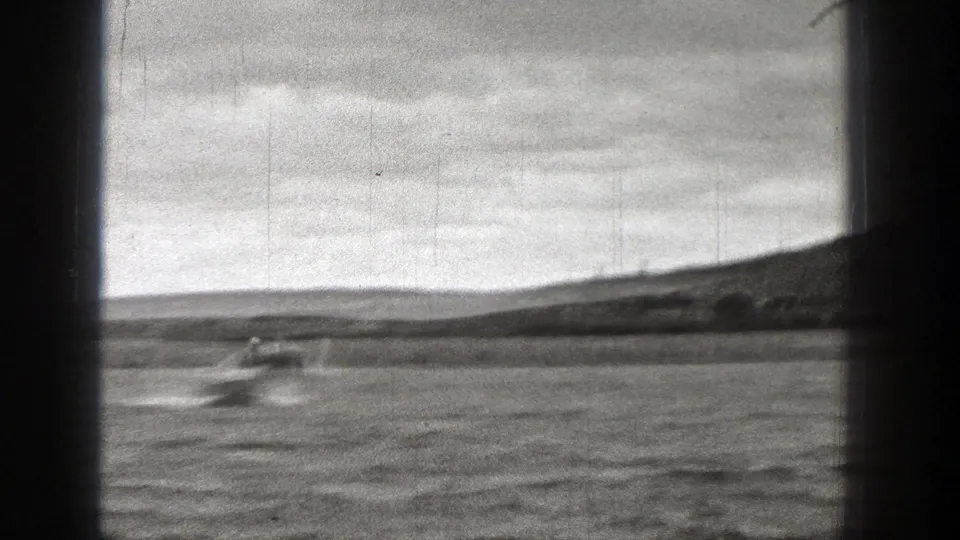 1938 Washington home-movie frame of a small motorboat accelerating across rippled water, leaving a white wake near the horizon.