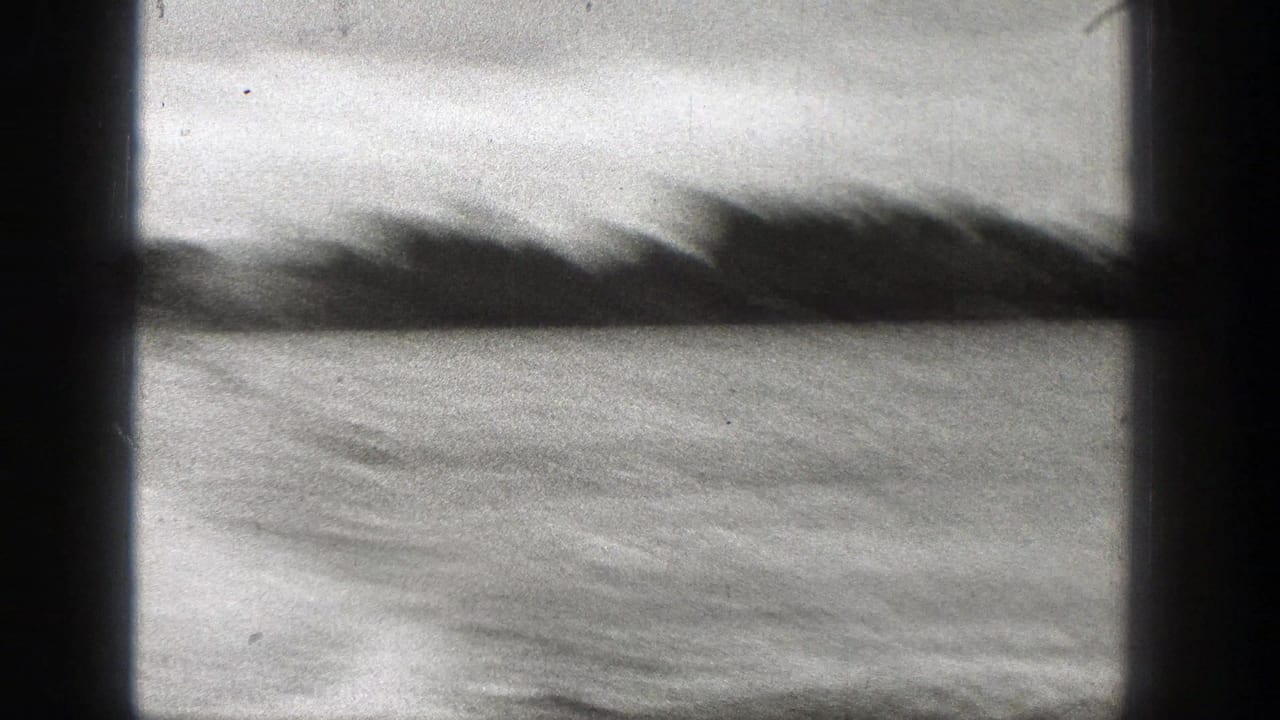 Soft 1938 Washington 8mm frame of rippled water and a blurred shoreline, with strong dark gate borders and film texture.
