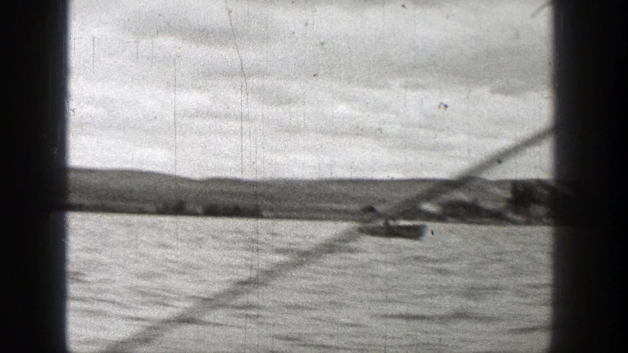 A small boat appears near a low shoreline in this soft 1938 Washington 8mm boating view.