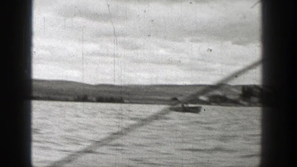 A small boat appears near a low shoreline in this soft 1938 Washington 8mm boating view.