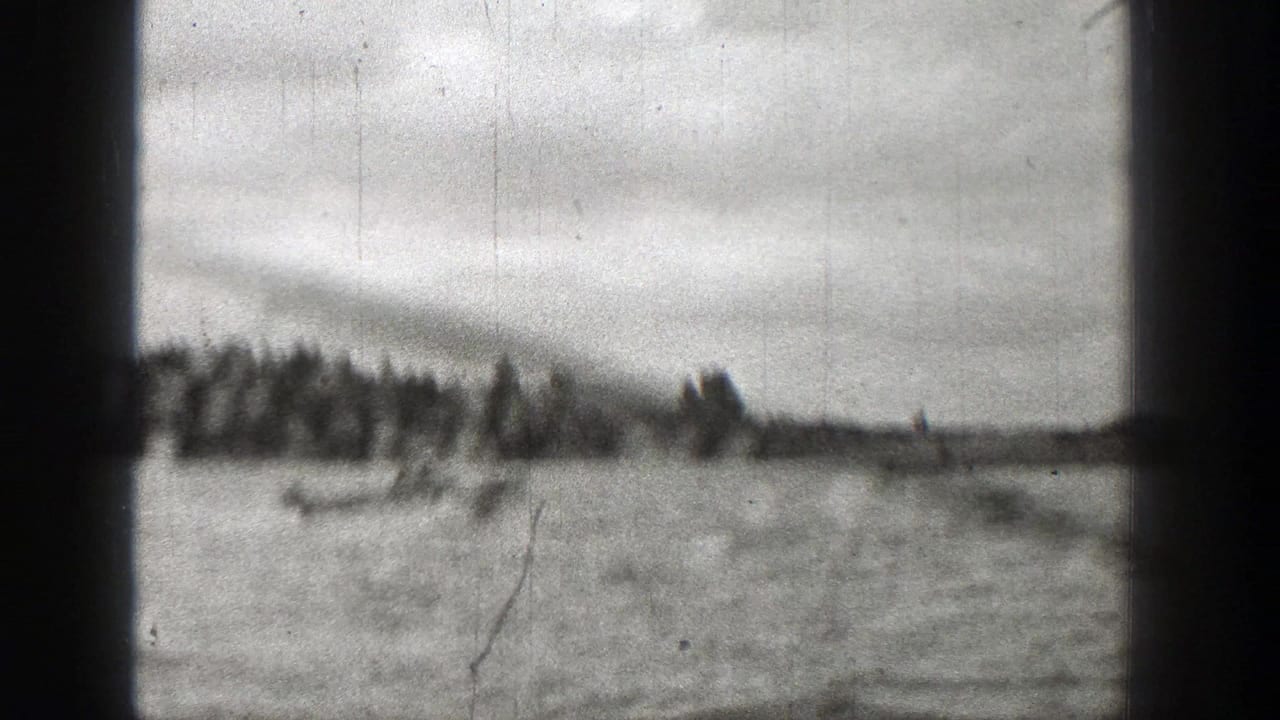 Late-1930s 8mm frame of a small boat on open water with trees and cloudy sky in the background.