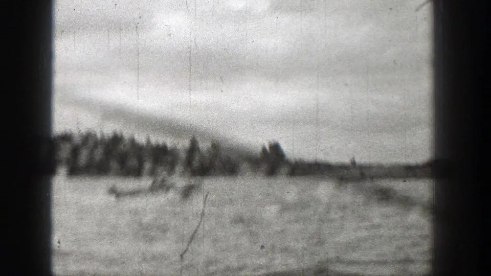 Late-1930s 8mm frame of a small boat on open water with trees and cloudy sky in the background.