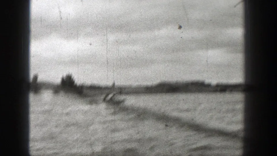 1938 Washington 8mm frame showing a small motorboat on a broad body of water, with a distant shoreline and dark camera borders.