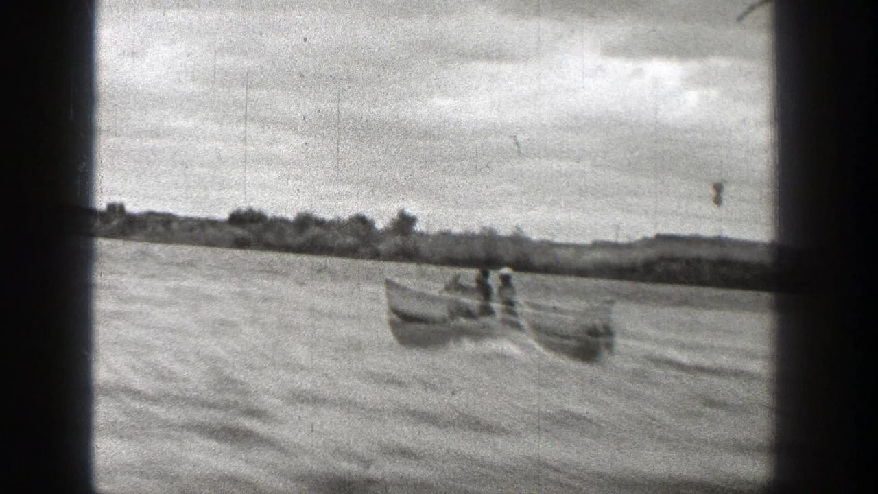 1938 Washington 8mm frame showing a small boat carrying people across a river with a low tree-lined shore beyond.