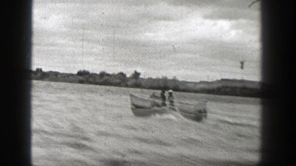 1938 Washington 8mm frame showing a small boat carrying people across a river with a low tree-lined shore beyond.