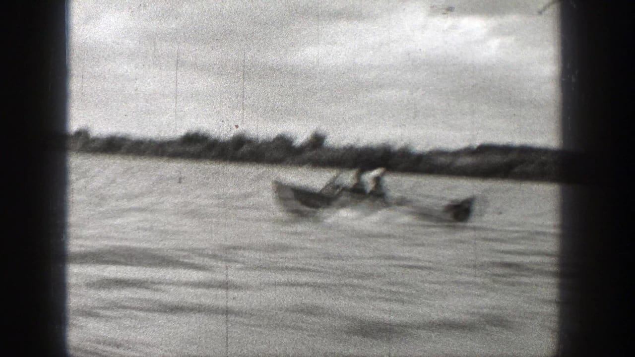 Small motorboat with people traveling rightward across open water.