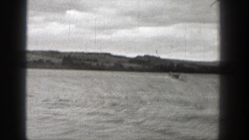 1938 Washington 8mm frame looking across open lake water toward a distant shore and low hills under a cloudy sky.