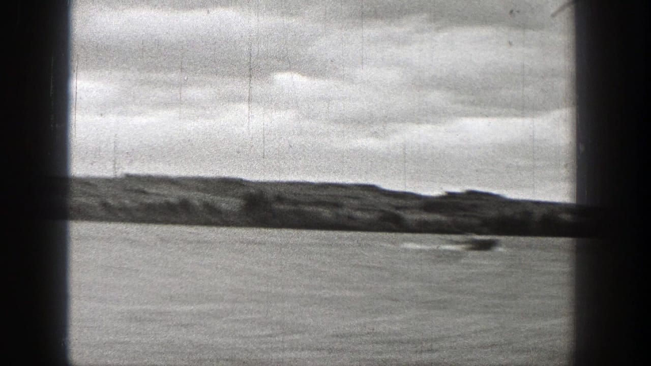 1938 Washington home-movie frame showing a small speedboat crossing a lake behind dark window or cabin framing.
