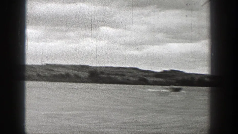 1938 Washington home-movie frame showing a small speedboat crossing a lake behind dark window or cabin framing.
