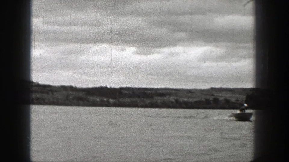 Black-and-white 8mm view of a Washington lake shoreline, with the speedboat mostly out of frame or distant.