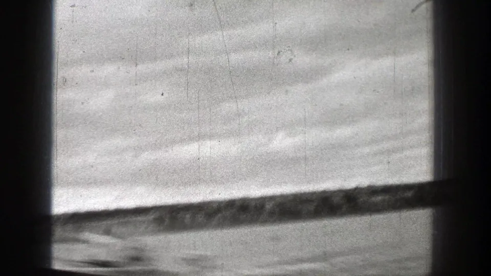 Black-and-white 8mm frame of a Washington lake and distant shoreline, divided by cabin-like vertical framing.