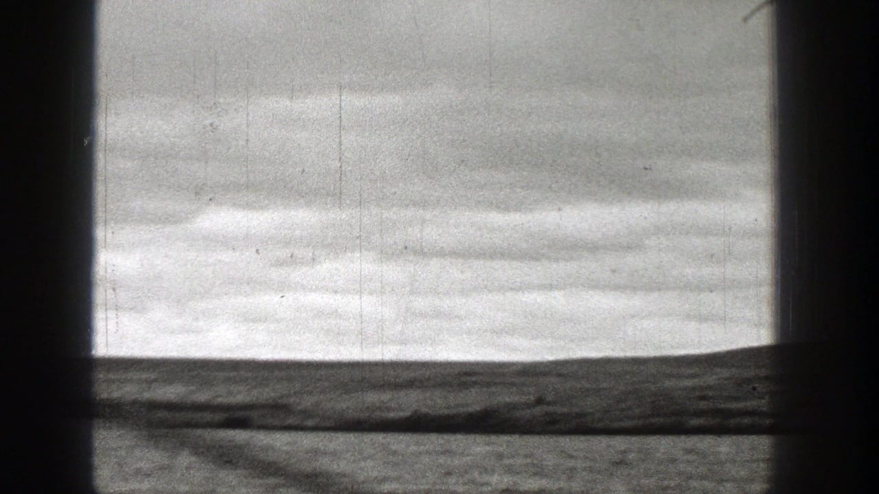 1938 Washington 8mm frame showing calm water, low shoreline, overcast sky, and dark vertical film-edge bands.