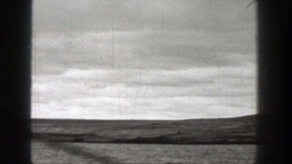 1938 Washington 8mm frame showing calm water, low shoreline, overcast sky, and dark vertical film-edge bands.
