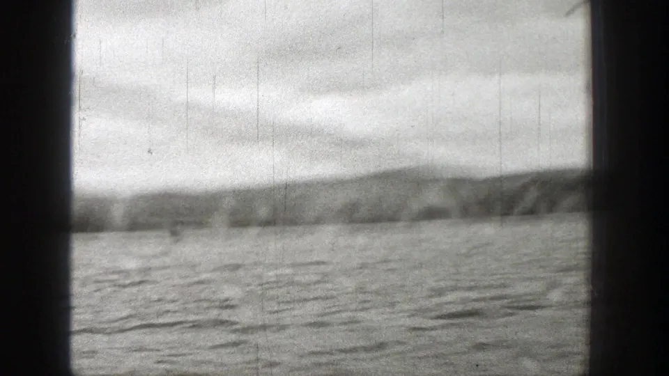Black-and-white 8mm frame of water, distant land, and cloudy sky from a moving vessel in Washington, 1938.
