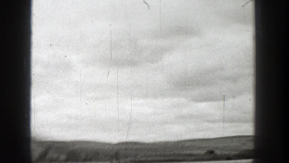 Black-and-white Washington coastal view with cloudy sky, low shoreline, and dark vessel frame elements, filmed in 1938.