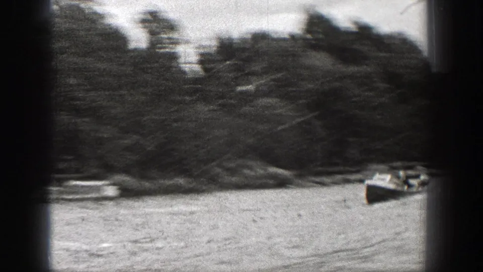 1938 Washington 8mm frame showing a motorboat with indistinct occupants moving along a wooded lake edge.