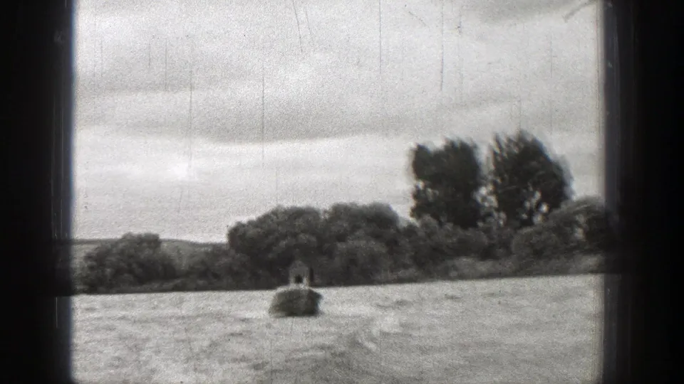 1938 Washington 8mm frame with rippled water, an indistinct small craft-like shape, shoreline trees, and cloudy sky.
