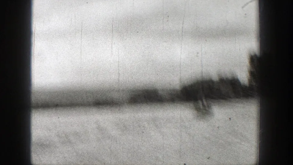 Soft black-and-white 8mm view of open water with a distant Washington shoreline partly obscured by a dark frame edge.
