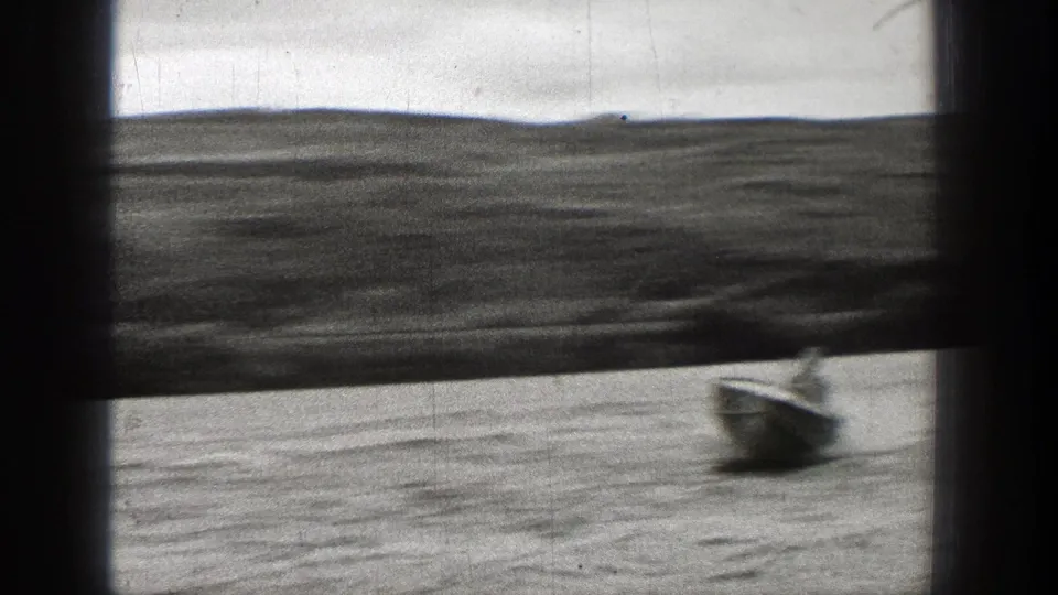 Black-and-white 1938 Washington frame with a small boat on choppy water below a distant shore and low hills.