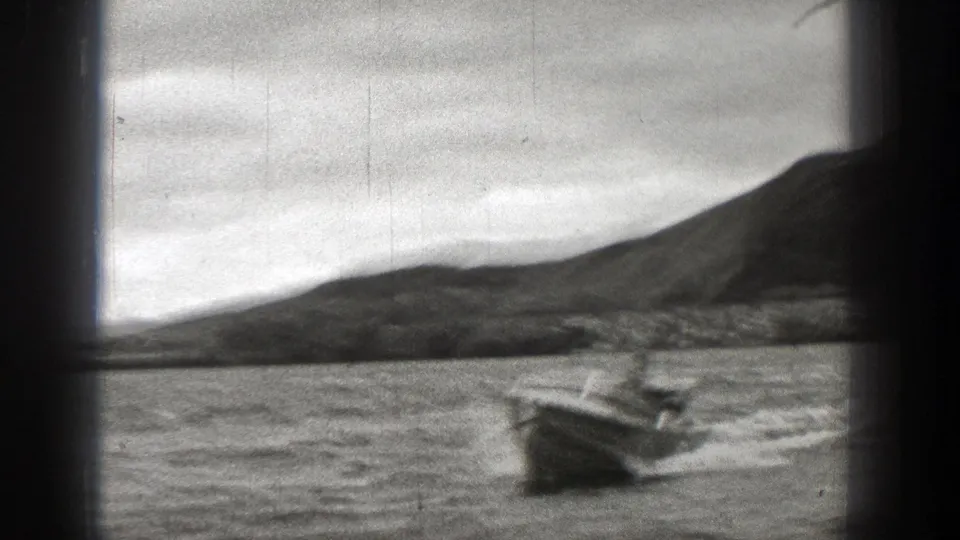 1938 Washington 8mm frame showing a small boat moving across rough water, with a dark hillside and cloudy sky behind it.