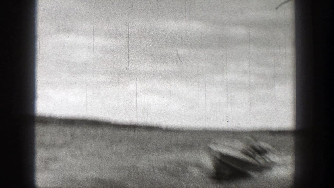 Blurred motorboat crossing a lake with dark scan edges and low hills in the distance.