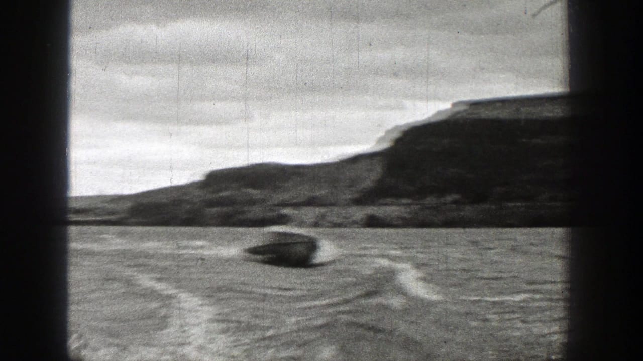 1938 Washington 8mm frame of a small motorboat speeding over rippled lake water with hills along the far shore.