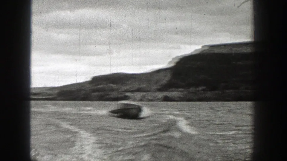 1938 Washington 8mm frame of a small motorboat speeding over rippled lake water with hills along the far shore.
