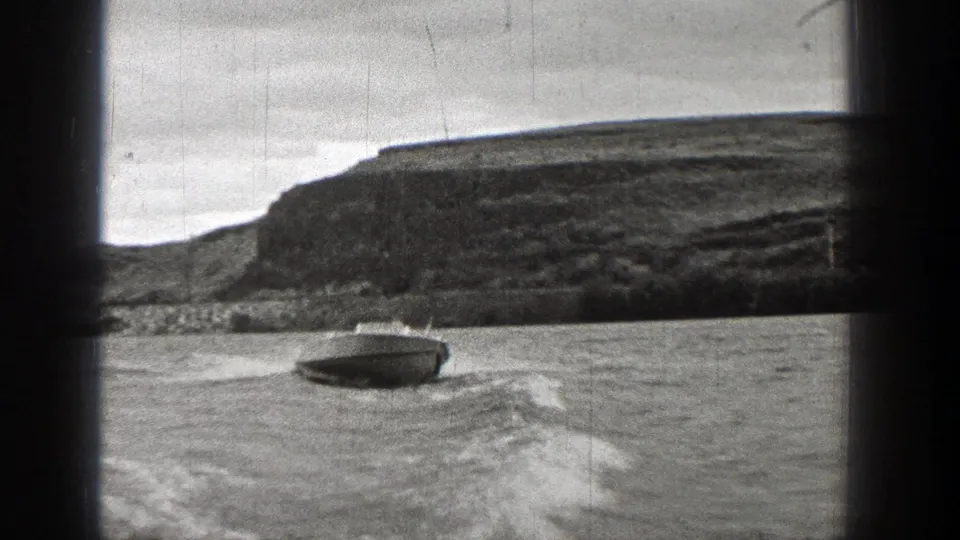 1938 Washington 8mm frame showing a motorboat near the lower edge of the lake, backed by a broad hilly shoreline.