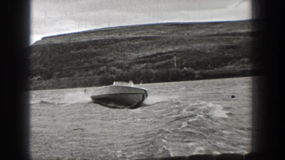 1938 Washington 8mm frame of a small motorboat moving fast across a lake, with white spray, wake, and hilly terrain behind.
