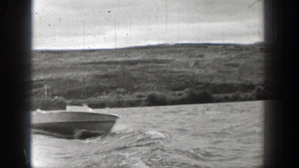 Washington 1938 home-movie frame showing a small speedboat crossing choppy water near a low shoreline, with dark film borders visible.