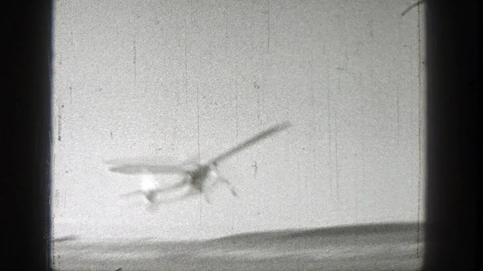 A small aircraft appears blurred against a pale sky in 1938 8mm footage identified as Washington by metadata.