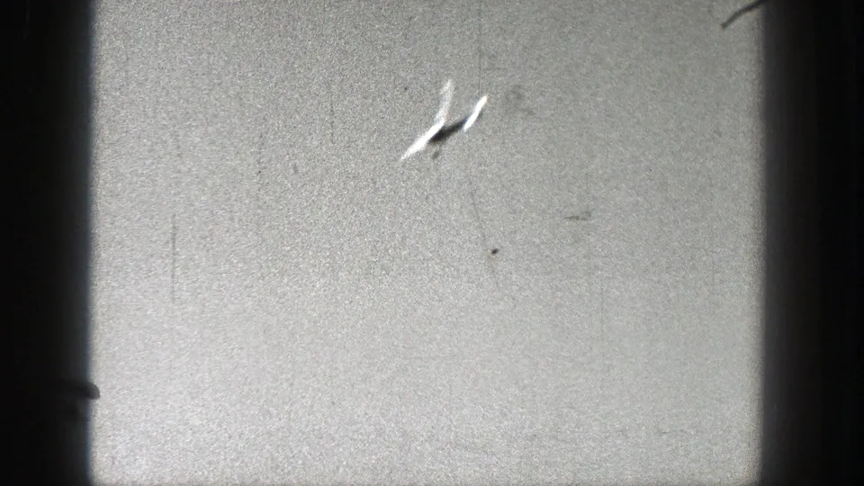 A small light aircraft climbs at an angle against gray sky in 1938 Washington 8mm home-movie footage.