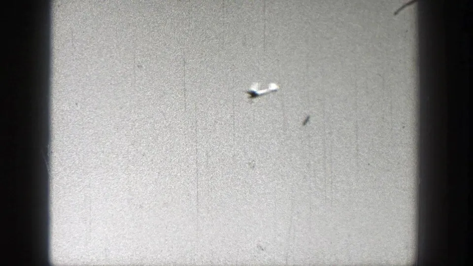 A distant small plane appears near the center of a grainy sky frame, with dark 8mm edge vignetting visible.