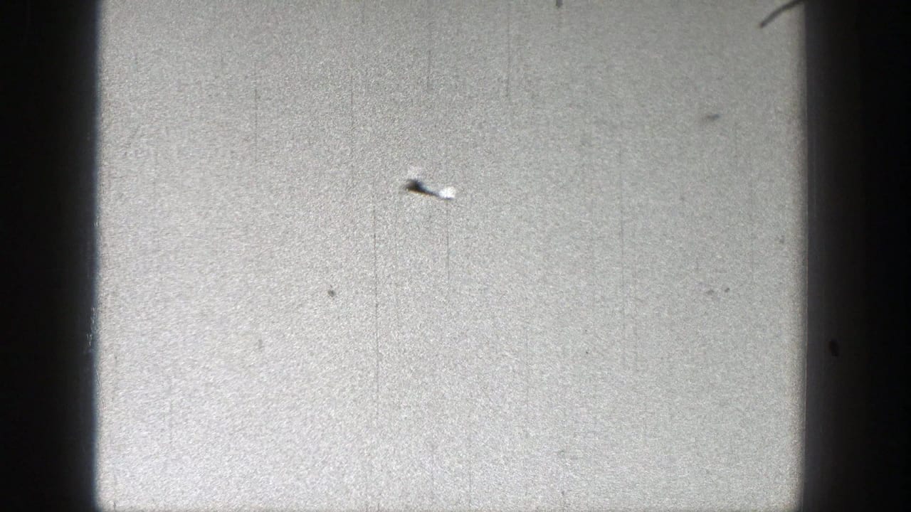Small toy glider crossing a pale sky with film grain and contact-sheet borders.