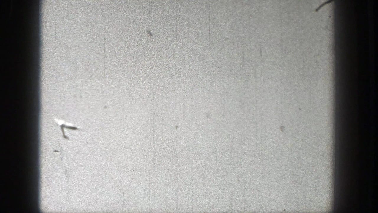 Tiny glider shape near the center of a pale, scratched sky frame.