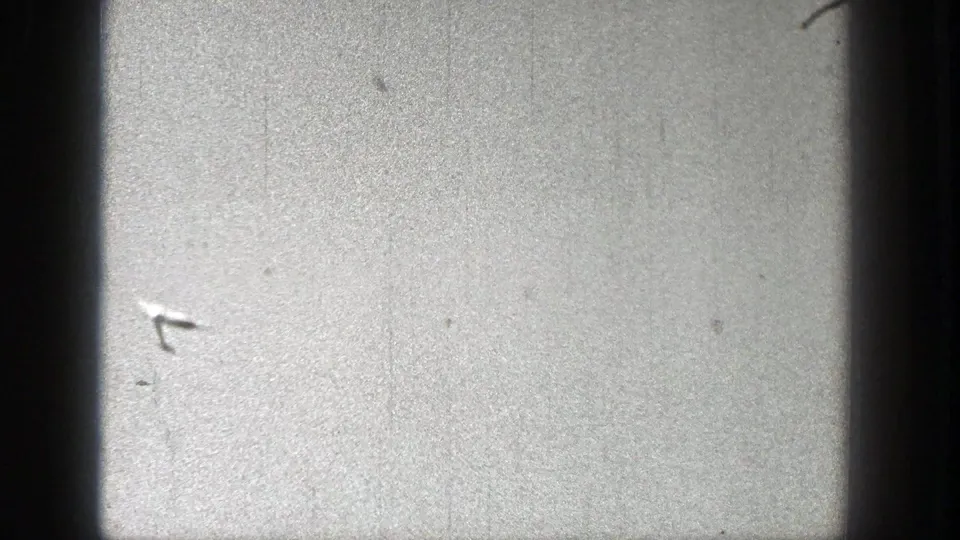 The toy glider is faintly visible near the middle of the sky, with grain, scratches, and contact-sheet borders from the 8mm scan.