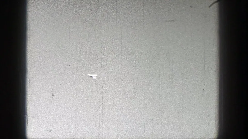 The white model airplane moves across a textured sky, framed by 8mm film scratches and edge shadows from the scan.