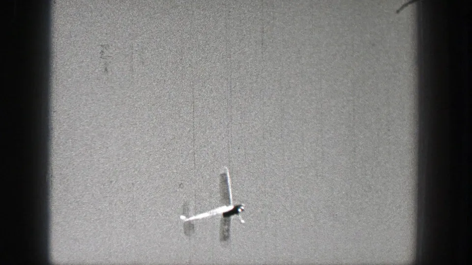 The white model airplane is most distinct near the lower right of the sky, with monochrome 8mm texture and scan-edge shadows visible.