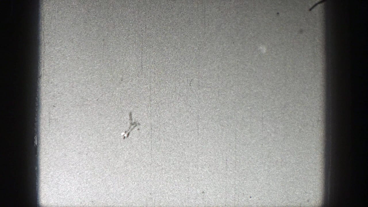 Small dark airplane silhouette against a bright grainy sky.