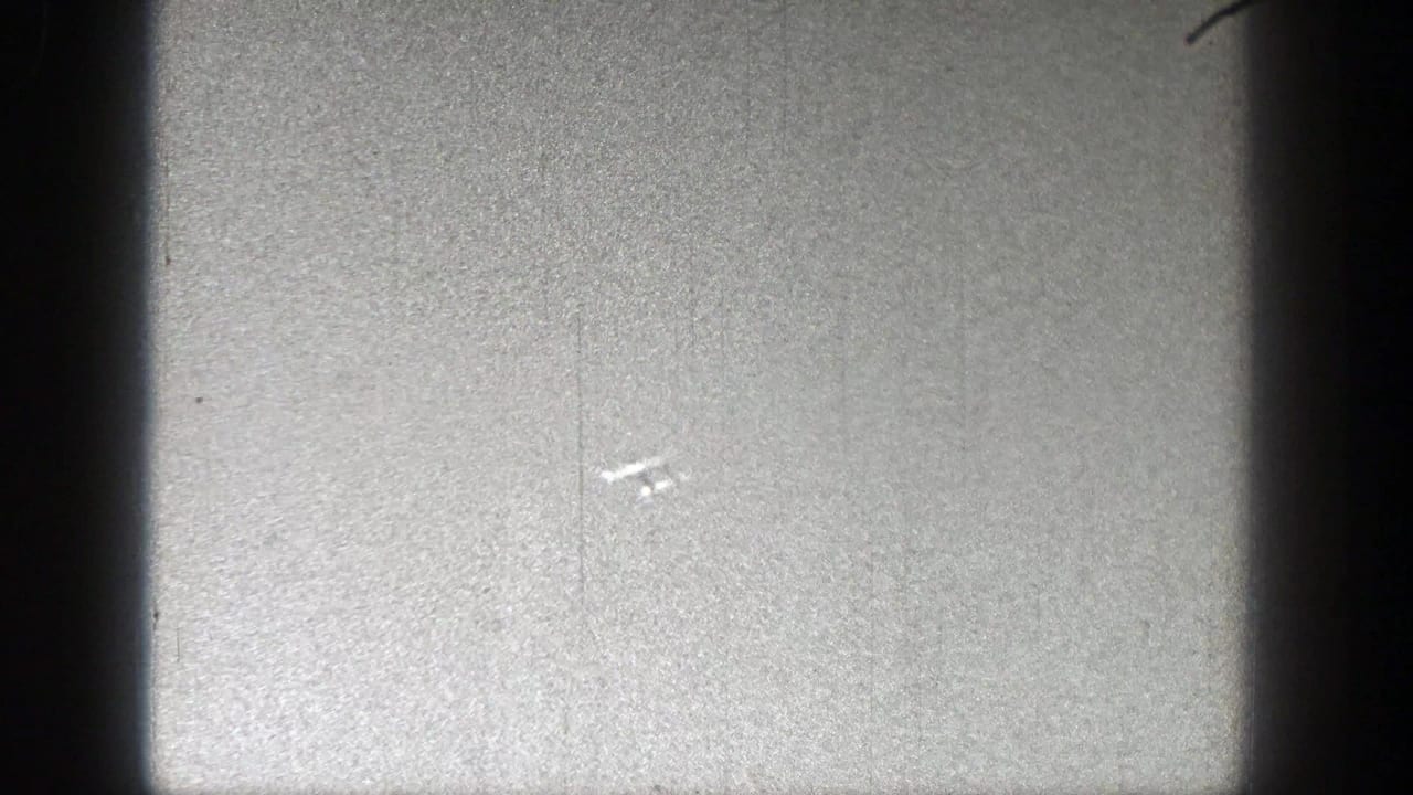 Tiny aircraft shape in a bright sky with visible film scratches.
