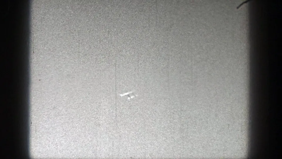 The aircraft remains small against the sky, with 8mm grain, scratches, and dust visible across the frame.