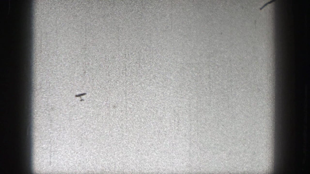A small dark object resembling a model plane appears against a pale grainy sky in 1938 Washington home-movie footage.
