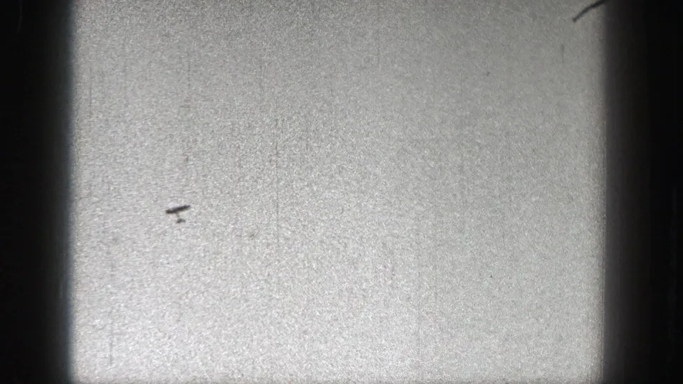 A small dark object resembling a model plane appears against a pale grainy sky in 1938 Washington home-movie footage.